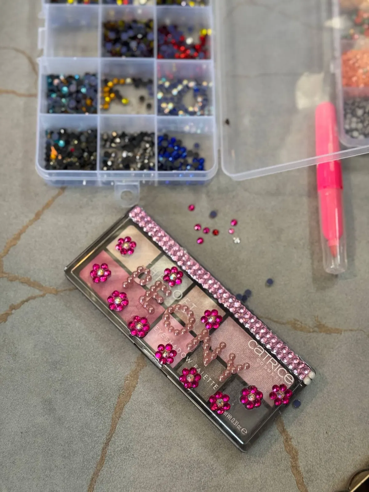 A box of coloured rhinestones beside a rhinestone-covered eyeshadow palette