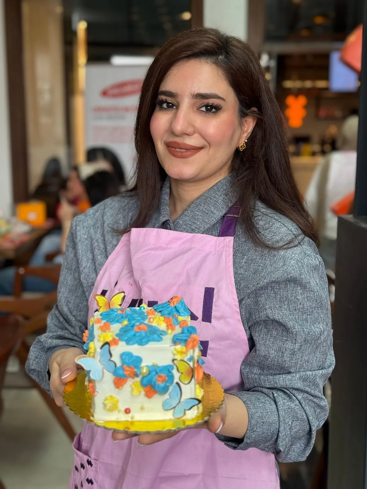 مشاركة بمريلة وردية تحمل كعكة زيّنتها بالفراشات
