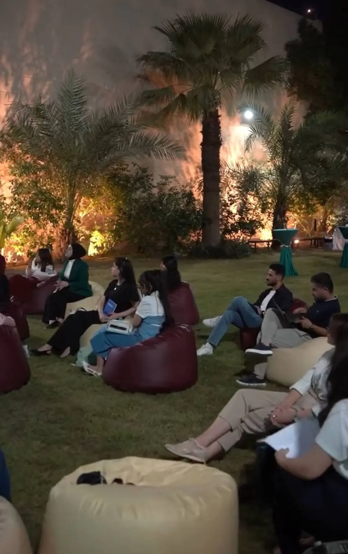 الحاضرات يجلسن على وسائد في حديقة مضاءة ليلاً