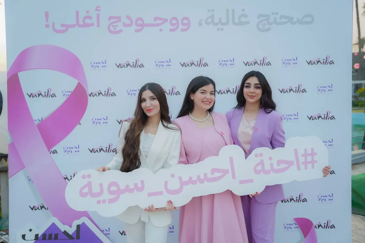 ثلاث مشاركات يحملن لافتة «#احنة_احسن_سوية» أمام خلفية الشريط الوردي